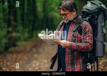 Looking for the way, using map. Hiking experience, senior man is in the forest at daytime. Stock Photo
