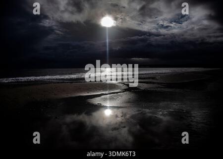 DRAMATIC EVENING WINTER VIEW OF A STORMY DESERTED BEACH IN DORSET UK WITH DARK MENACING CLOUDS AND A SHAFT OF SUNLIGHT ILLUMINATING WATER ON THE BEACH. Stock Photo