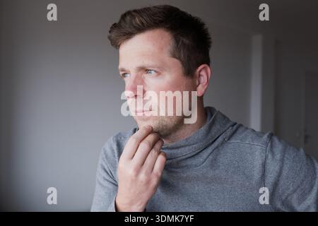 Pensive young man standing at home thinking about problems and making decisions Stock Photo