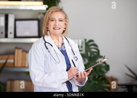 Senior Female Doctor In White Lab Coat With Clipboard In Office Setting, Professional Medical Portrait Stock Photo