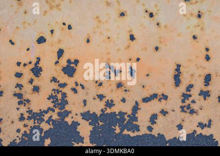 A macro texture shot of a weathered metal sheet showing heavy oxidation, rust spots, and dark blue-grey corrosion patterns on an orange background Stock Photo