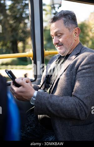 Mature man commuting, using smartphone and earphones on public transport Stock Photo