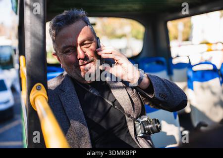 Mature man talking on phone riding sightseeing bus Stock Photo