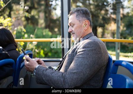 Mature man commuting on bus using smartphone and earbuds Stock Photo