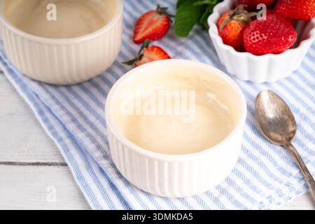 Vanilla or white chocolate pudding dessert, in ceramic portioned bowl on kitchen table, with fresh strawberries Stock Photo