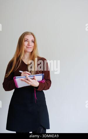 Thoughtful woman writing notes in notebook against minimal background, copy space Stock Photo