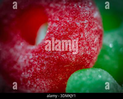Macro of colorful sugar-coated gummy candies showing crystal texture and bright red and green tones in soft focus close-up detail. Stock Photo