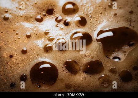 Close-up of soft drink foam with textured bubbles showing rich brown tones and glossy reflections under warm ambient light. Stock Photo