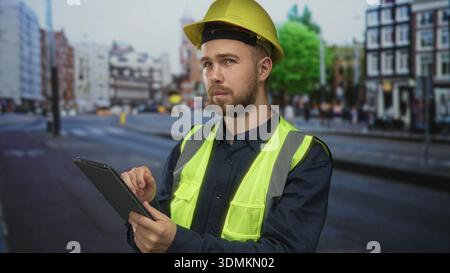 Man builder in hardhat and reflective vest taps tablet on street for site management; planning concentration. Stock Photo