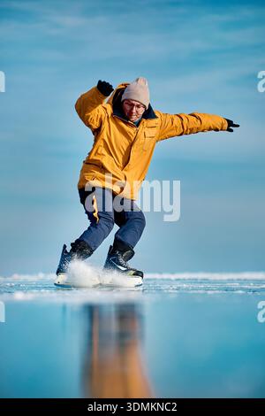 Man athlete in yellow jacket ice skating on frozen lake with reflection at winter time Stock Photo