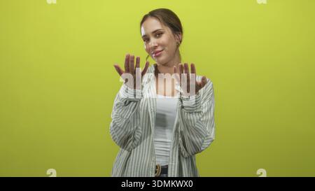 Woman beckons with hands and palms forward, wearing striped shirt and white tank in green studio; invitation warmth. Stock Photo