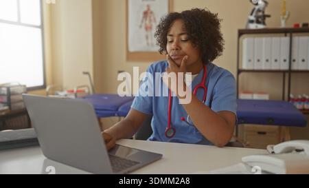 African american woman doctor with hand on chin looking at laptop in clinic building; thinking concern. Stock Photo