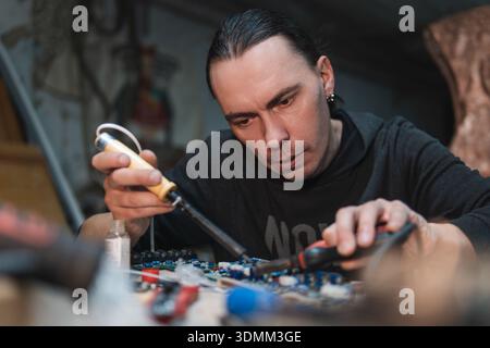 a man with a soldering iron repairs equipment in a workshop, Stock Photo