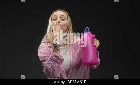Woman holding bright pink detergent bottle with hands, smiling and offering the bottle toward camera in studio set; freshness joyful. Stock Photo