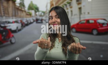 Woman beckons with hands on street in green longsleeve top near parked car; invitation welcome connection. Stock Photo