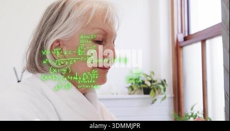 Standing senior woman in home bathroom wearing white bathrobe, studying green hologram equations Stock Photo