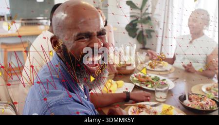 Laughing mature bald bearded man wearing blue shirt at home dining table, showing AR mesh Stock Photo