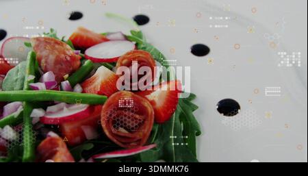 Displaying salad resting on white plate in studio, with greens, strawberries, prosciutto, balsamic Stock Photo