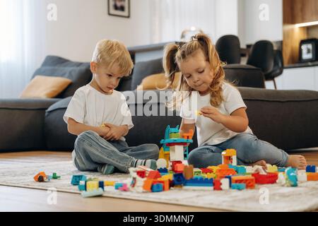 Building the tower, sitting. Two kids are playing with construction blocks toys at home. Stock Photo