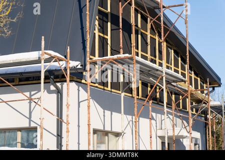 Scaffold structure on residential building facade during renovation, black roof panels and unfinished wall grid, close view of construction work and m Stock Photo
