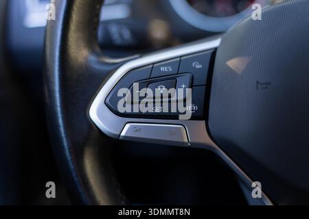 Detail of car steering wheel spoke with multifunction buttons for cruise control and speed limiter, on off switch, textured leather rim and silver tri Stock Photo