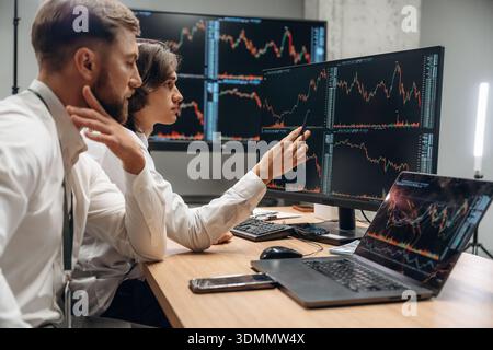 Crypto and stock graphs are on the screens. Two male exchange workers are in the office together. Stock Photo