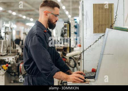 Focused, working by machine, the operator. Warehouse worker in an industrial environment of a factory or storage area. Stock Photo