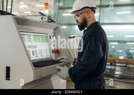 Focused, working by machine, the operator. Warehouse worker in an industrial environment of a factory or storage area. Stock Photo