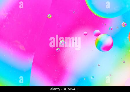 Abstract macro photography of oil bubbles floating on water surface with vibrant pink and turquoise gradient background Stock Photo
