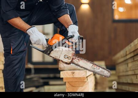 Using a chainsaw. Close-up of a carpenter working with wood using professional tools in a workshop. Stock Photo
