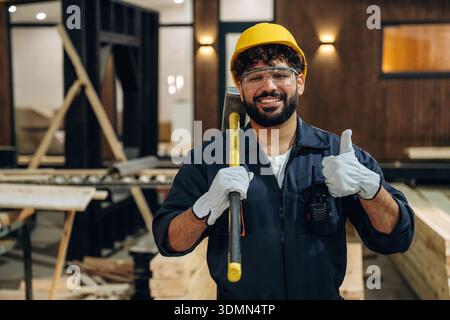 Everything is fine, showing thumb up. Portrait of a male carpenter posing in a woodworking workshop. Stock Photo
