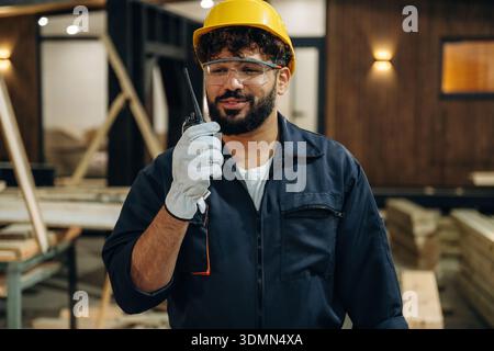 Talking by walkie talkie. Portrait of a male carpenter posing in a woodworking workshop. Stock Photo