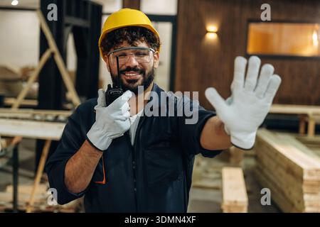 Talking by walkie talkie. Portrait of a male carpenter posing in a woodworking workshop. Stock Photo
