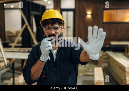 Talking by walkie talkie. Portrait of a male carpenter posing in a woodworking workshop. Stock Photo