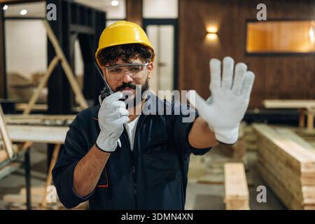 Talking by walkie talkie. Portrait of a male carpenter posing in a woodworking workshop. Stock Photo