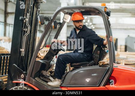 Driving, skilled employee. Warehouse worker operating a forklift while handling wooden materials. Stock Photo