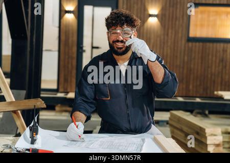 Magnifying glass, holding and looking through it. Portrait of a male carpenter posing in a woodworking workshop. Stock Photo