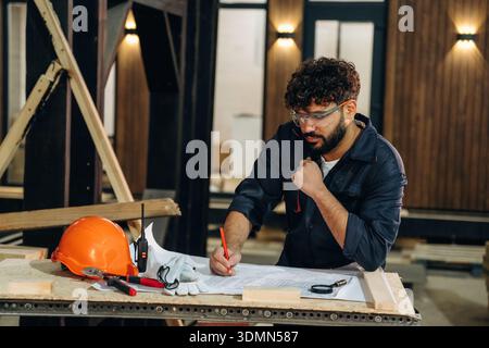 Smart engineer is working with plan. Male carpenter working with wooden materials in a professional workshop. Stock Photo
