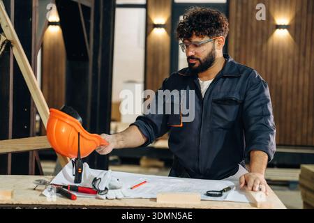 Smart engineer is working with plan. Male carpenter working with wooden materials in a professional workshop. Stock Photo