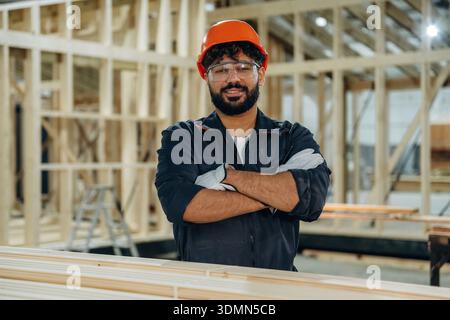 Arms crossed, standing. Portrait of a male carpenter posing in a woodworking workshop. Stock Photo