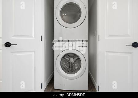 White washing machine is in a small space between two doors. The space is narrow and the machine is tall Stock Photo