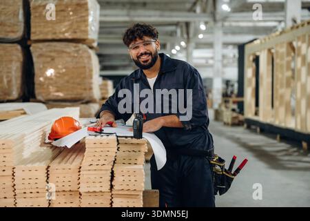 Writing on the paper, engineer is with plan. Male carpenter working with wooden materials in a professional workshop. Stock Photo