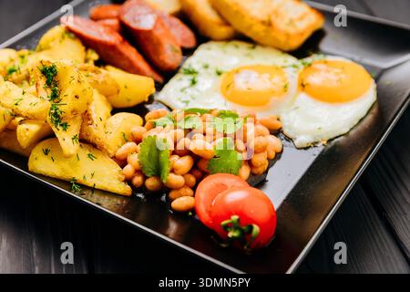 Full breakfast plate with fried eggs, sausages, potatoes, beans and toast on dark table Stock Photo