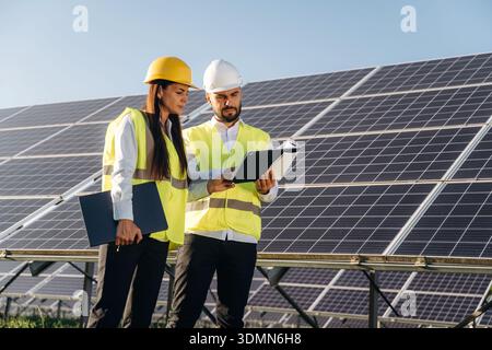 Two solar engineers standing together at a photovoltaic field, in bright safety vests. Stock Photo