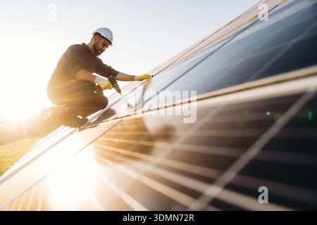 Installation, using the drill. Male solar engineer examining photovoltaic panels at a power station. Stock Photo