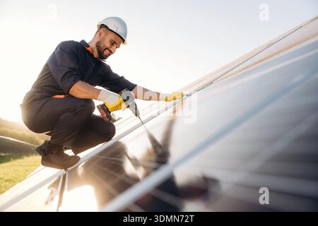 Installation, using the drill. Male solar engineer examining photovoltaic panels at a power station. Stock Photo