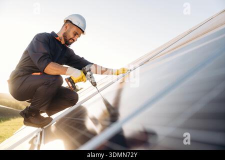 Installation, using the drill. Male solar engineer examining photovoltaic panels at a power station. Stock Photo