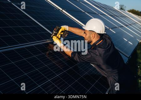 Side view, installing process. Male solar engineer examining photovoltaic panels at a power station. Stock Photo