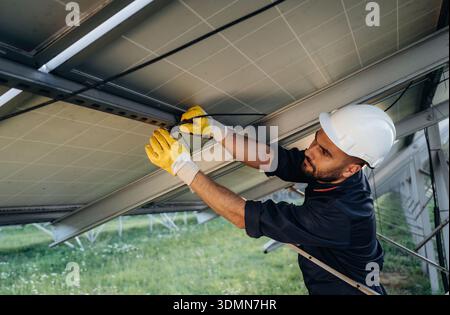 Strong construction, under the surface, installation. Male solar engineer examining photovoltaic panels at a power station. Stock Photo