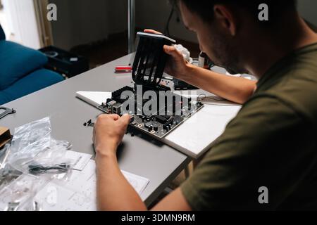 Back view of computer technician male installing CPU cooler onto motherboard, performing maintenance or upgrade in specialized workshop environment. Stock Photo